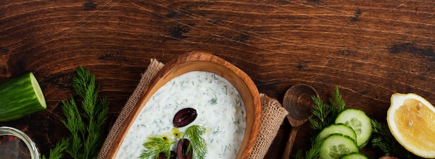 Traditional Greek sauce Tzatziki in olive wooden bowl on old rustic background. Top view.