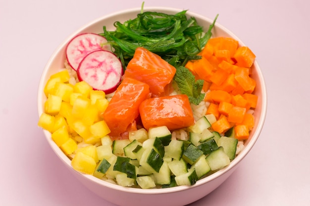 Traditional Hawaiian red fish poke bowl with rice, radish,cucumber, tomato, and seaweeds. Buddha bowl. Diet food. Flat lay. Pink background.