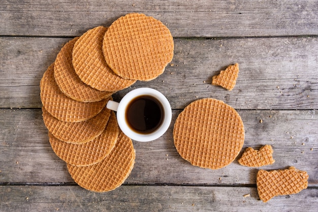 Traditional Holland waffles with caramel and cup of coffee on the wooden background, top view.