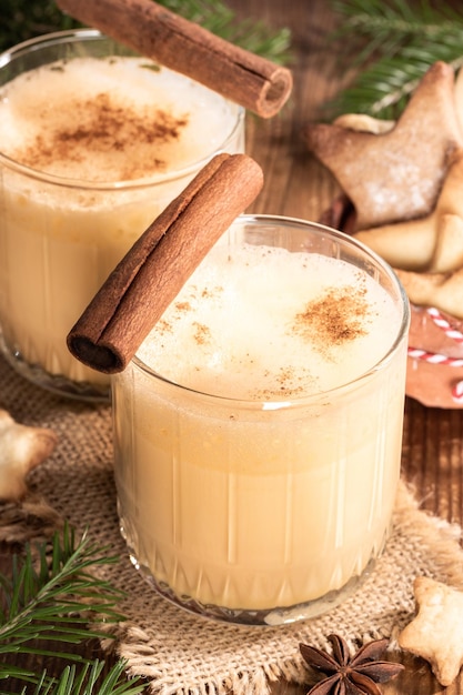 Traditional homemade Christmas drink eggnog with cinnamon in two glasses on burlap on wooden table