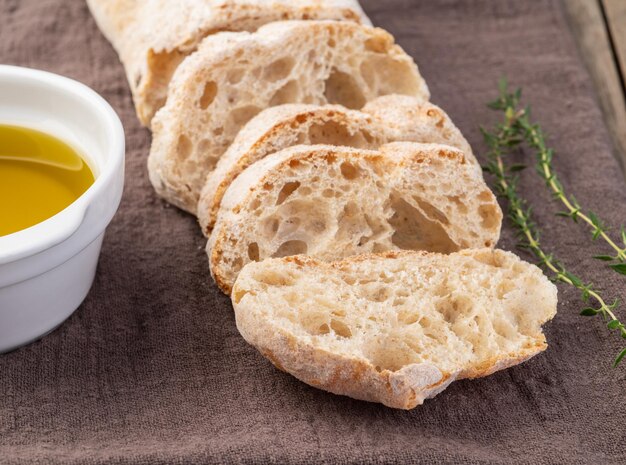 Традиционный домашний хлеб чиабатта с ломтиками и оливковым маслом на деревянном столе