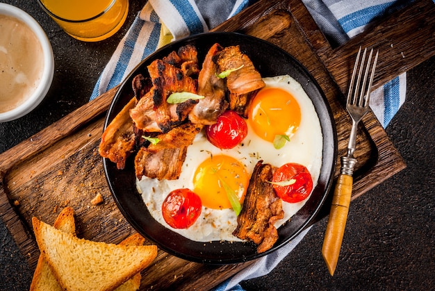 Traditional homemade english american breakfast, fried eggs, toasts, bacon, with coffee mug and orange juice