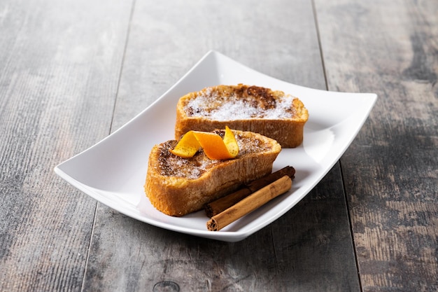 Traditional homemade Spanish torrijas decorated with cinnamon and Orange peel on wooden table