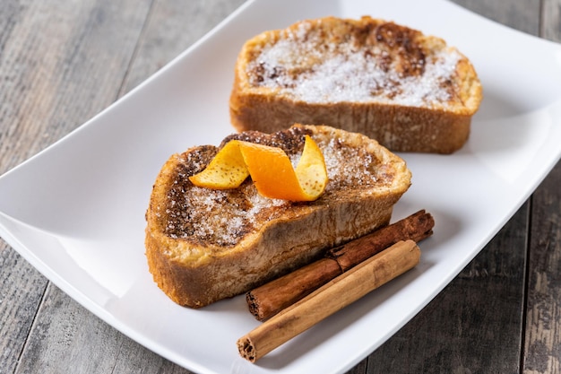 Traditional homemade Spanish torrijas decorated with cinnamon and Orange peel on wooden table