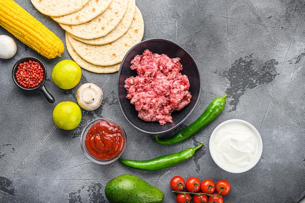 Traditional homemade taco ingredients with meat over grey background top view