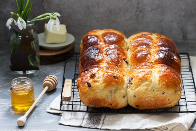 Traditional hot cross buns with honey and butter on a concrete background.