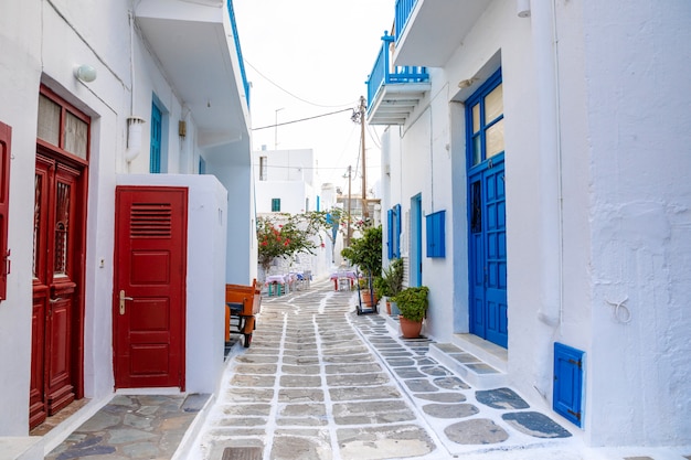 ミコノス島、ギリシャのギリシャの村の狭い通りに青いドアと窓のある伝統的な家屋