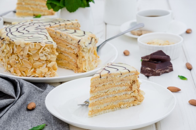 Torta esterhazy ungherese tradizionale su un piatto bianco su un tavolo di pietra con una tazza di caffè, menta e mandorle.