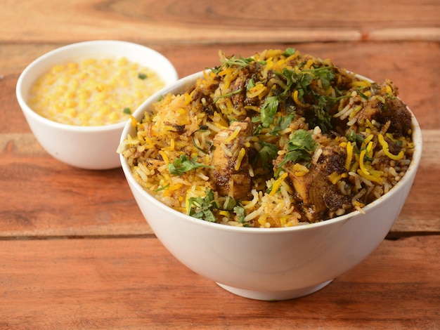 Foto tradizionale pollo hyderabadi dum biryani a base di riso basmati cotto con spezie masala servito con fuoco selettivo boondi raita