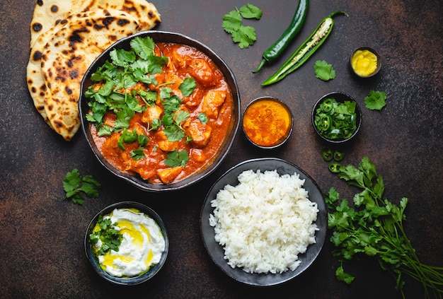 전통적인 인도 요리 치킨 티카 마살라, 그릇에 매운 카레 고기, 바스마티 쌀, 빵 난, 요거트 라이타 소스를 소박한 어두운 배경, 꼭대기 전망이 닫힙니다. 위에서 인도 스타일의 저녁 식사
