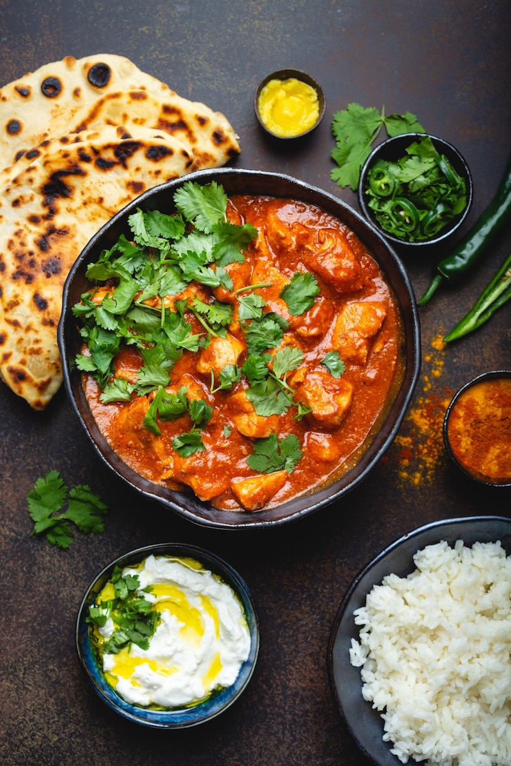 Photo traditional indian dish chicken tikka masala with spicy curry meat in bowl, basmati rice, bread naan, yoghurt raita sauce on rustic dark background, top view, close up. indian style dinner from above