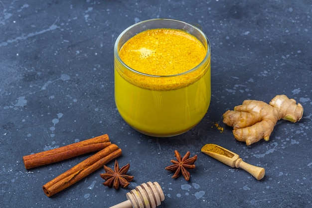 Traditional Indian drink turmeric milk is golden milk in glass mug with  turmeric and root ginger, cinnamon, anis star on dark background. Weight loss, healthy and organic drink. Close up