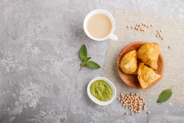 Samosa indiano tradizionale dell'alimento in piatto di legno con chutney di menta su un copyspace concreto grigio. vista dall'alto.