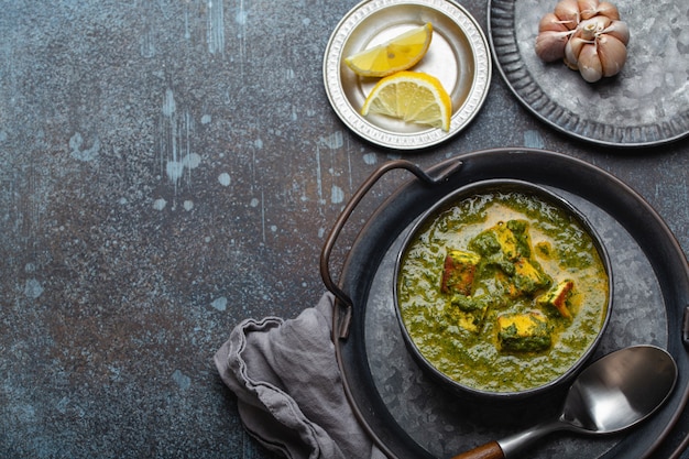 Traditional Indian Punjabi food Palak Paneer with spinach and cheese in vintage metal bowl with spoon on rustic concrete background from above with space for text