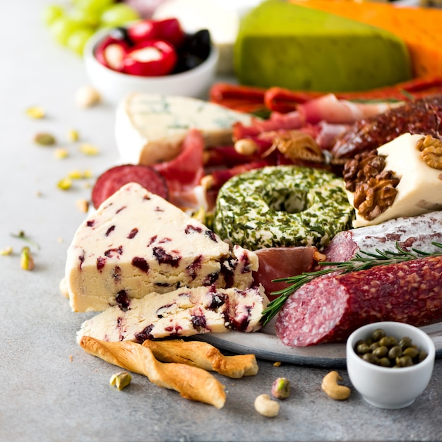 Photo traditional italian antipasto, cutting board with salami, cold smoked meat, prosciutto, ham, cheeses, olives, capers on grey background. cheese and meat appetizer. square crop