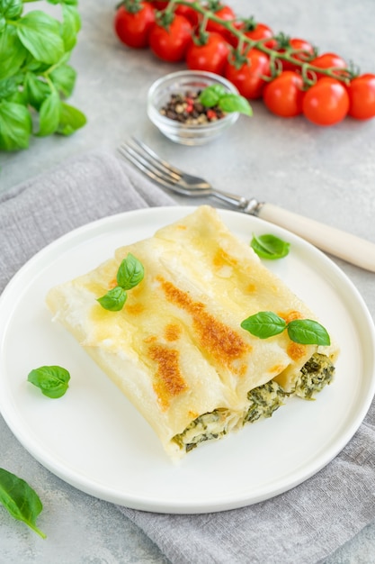 Traditional Italian cannelloni with ricotta and spinach in bechamel sauce with fresh basil leaves