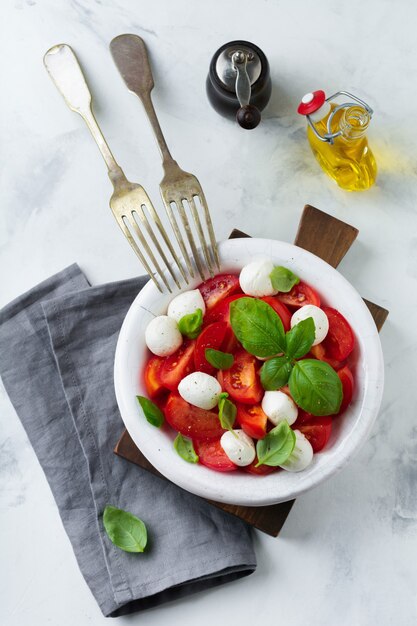 Traditional Italian caprese salad with tomatoes, maozzarella cheese and basil on a light marble surface in a white old ceramic plate