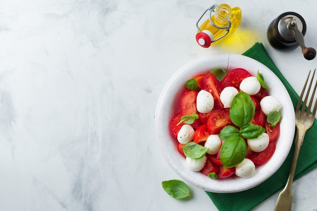 Traditional Italian caprese salad with tomatoes, maozzarella cheese and basil on a light marble surface in a white old ceramic plate