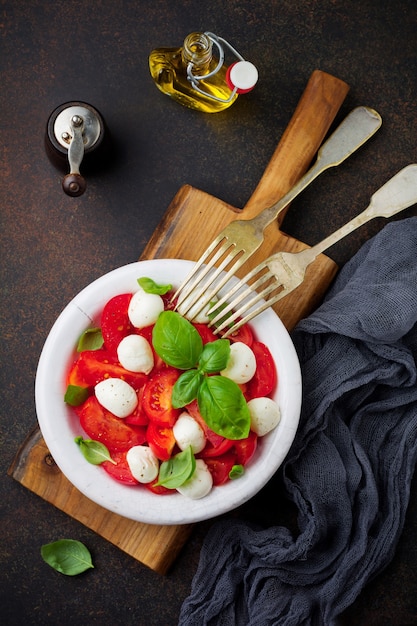 Traditional Italian caprese salad with tomatoes, mozzarella cheese and basil on dark surface in white old ceramic plate. Selective focus.Top view.