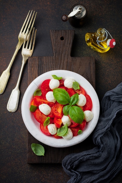 Traditional Italian caprese salad with tomatoes, mozzarella cheese and basil   in white old ceramic plate.  Top view.