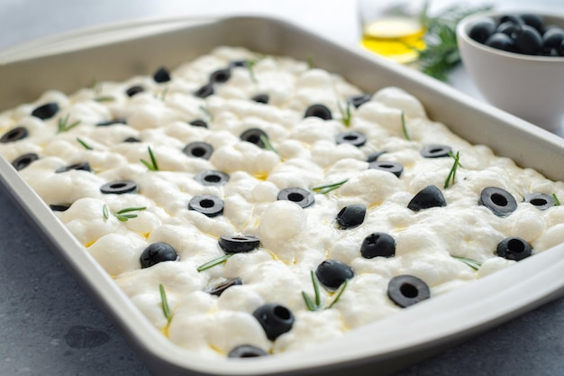 Traditional italian focaccia bread with rosemary and olives. raw focaccia dough is ready to be baked