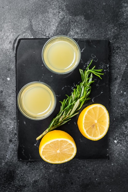 Traditional italian lemon alcohol drink liqueur limoncello with lemon and rosemary Black background Top view