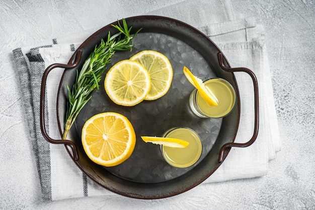 Фото Традиционный итальянский ликер лимончелло лимонный спирт пищеварительный с лимоном и розмарином белый фон вид сверху