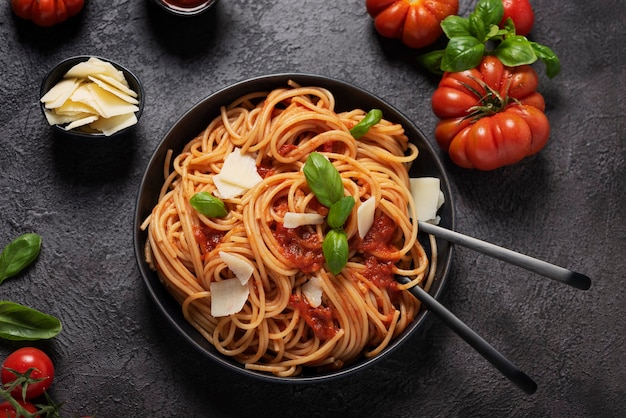 Pasta italiana tradizionale con salsa di pomodoro, basilico e formaggio su sfondo nero, vista dall'alto in basso con spazio di copia