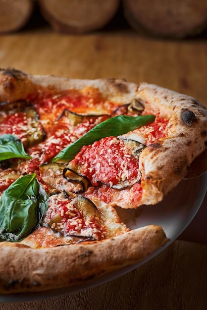 Pizza tradizionale italiana con melanzane, mozzarella, basilico e pomodori su fondo di legno