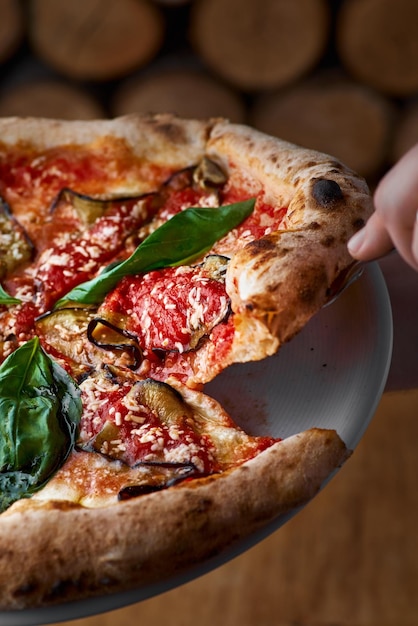 Traditional Italian pizza with eggplants mozzarella basil and tomatoes on wooden background