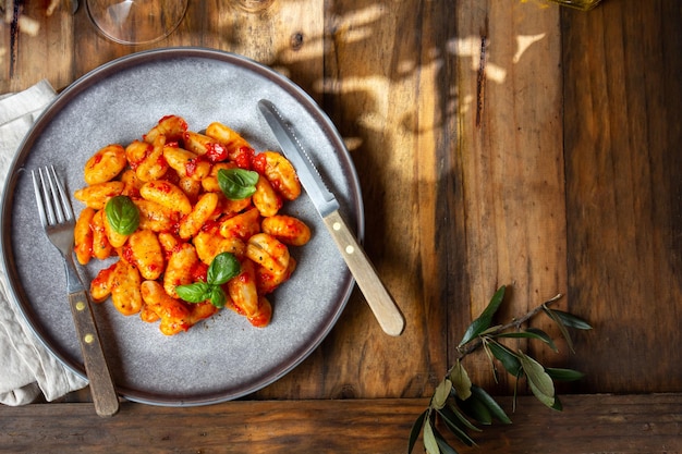 Traditional Italian potato Gnocchi with tomato sauce and fresh basil on blue plate on wooden background