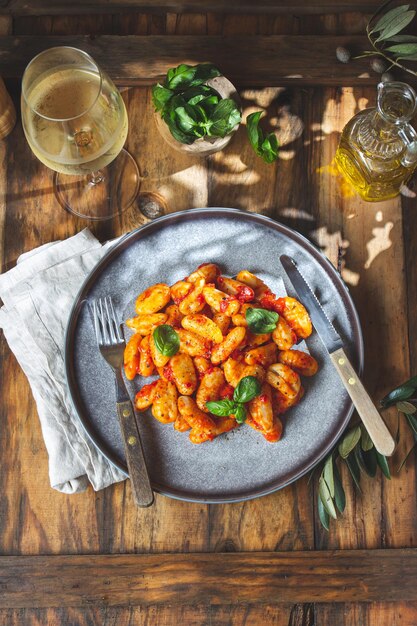 Traditional Italian potato Gnocchi with tomato sauce and fresh basil with glas of white wine rustic background