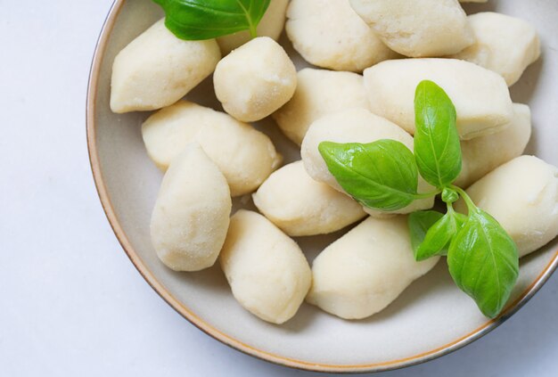 Traditional italian potato gnocci  (pasta) decorated with basil leaf, in ceramic plate. Uncooked pasta concept. Top View. Flat Lay