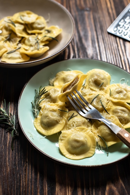 Traditional italian ravioli with rosemary and parmesan served on a rustic wooden table. Italian pasta