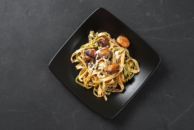 A traditional italian and roman dish fettuccini pasta with spinach and mushrooms on a black plate on