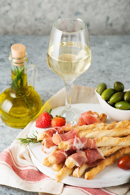 Traditional Italian snacks for wine, breadsticks (grissini), tomatoes, prosciutto (jamon), strawberries and olives. Selective focus.