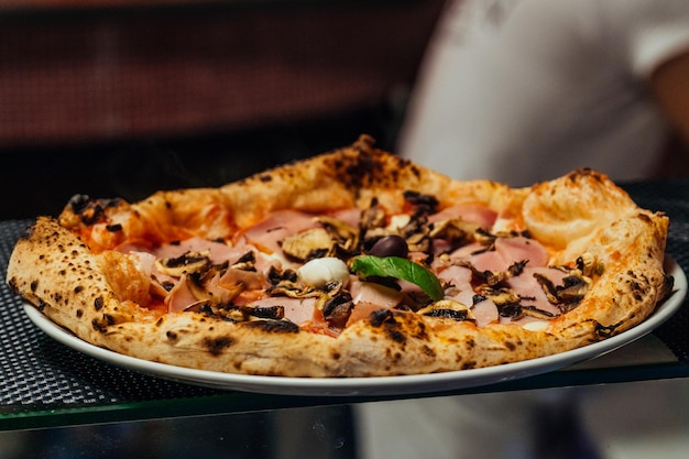 Foto pizza tradizionale in stile italiano con prosciutto e funghi fuori dal forno in mostra