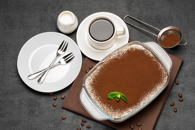 Traditional Italian Tiramisu dessert in glass baking dish and cup of fresh hot espresso coffee on concrete background or table