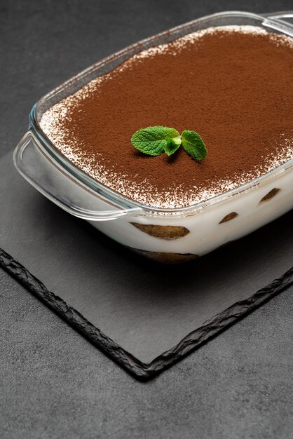 Traditional Italian Tiramisu dessert in glass baking dish on stone serving board on concrete background or table