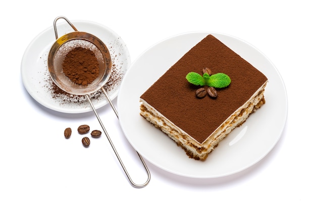 Традиционная итальянская квадратная десертная порция тирамису на керамической тарелке и ситечке с изолированным какао-порошком