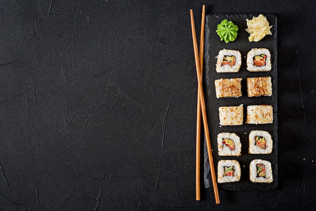 Foto cibo tradizionale giapponese - sushi, panini e bacchette per sushi su uno sfondo scuro. vista dall'alto