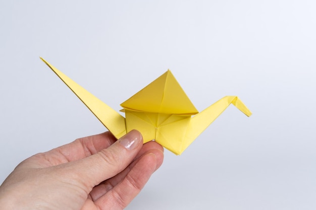 Traditional Japanese origami cranes made of yellow paper on a white background A hand holding a paper bird Children's creativity A symbol of peace