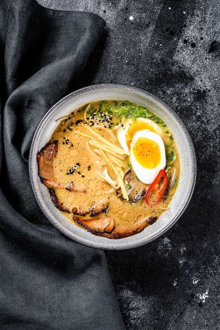 Фотография традиционный японский суп из рамена с мясным бульоном, азиатской лапшой, водорослями, нарезанной свининой, яйцами. черный фон. вид сверху