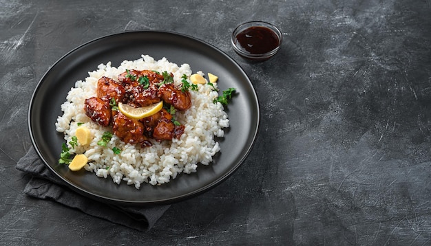 Traditional Japanese teriyaki chicken with rice, sesame seeds and fresh herbs on a dark background. Top view, copy space.