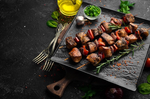 Traditional kebab juicy chicken kebab with vegetables on a\
black stone plate barbecue top view free space for text
