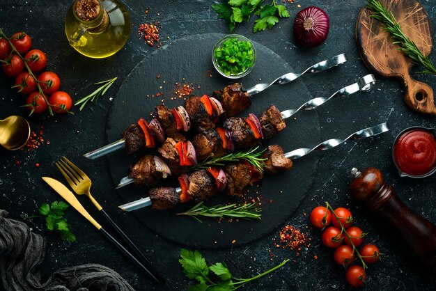 Traditional Kebab Juicy pork skewers with vegetables on a black stone plate Barbecue Top view Free space for text