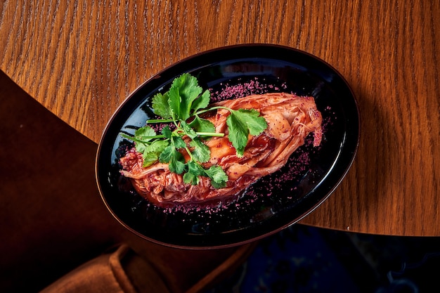 A traditional Korean dish is spicy Chinese cabbage kimchi with spices and hot sauce, served in a black plate on a wooden table. View from above