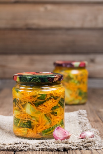 Traditional Korean snack of kimchi cucumbers in two glass jars: cucumbers marinated with carrots, hot pepper and garlic, with vegetable oil, on a napkin.