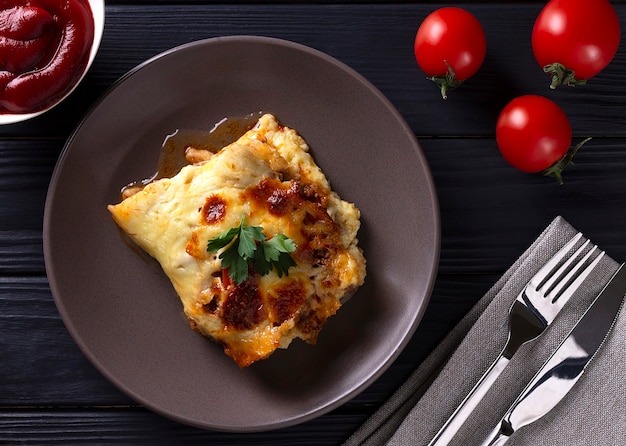 Traditional lasagna with cheese and tomatoes, in a plate, on a wooden table