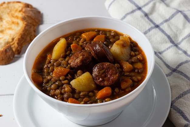 Traditional lentil soup with legs, carrots and chorizo on a white  plate on a white background